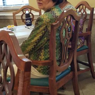 A woman sitting at a dining table, wearing vibrant attire.