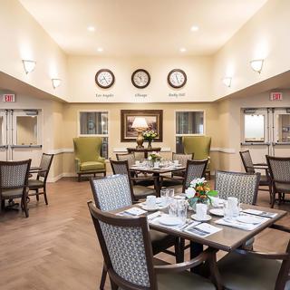 A well-lit dining room with neatly arranged tables and chairs, featuring elegant decor and multiple wall clocks.