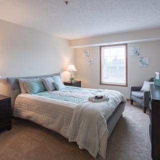 A cozy bedroom with a neatly made bed, bedside tables with lamps, and a window letting in natural light.