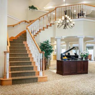 A spacious lobby featuring a grand staircase, chandelier, and a grand piano.
