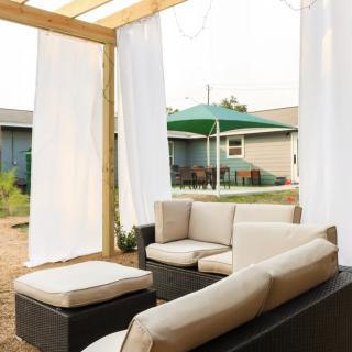 A cozy outdoor patio with comfortable sofa seating under a wooden pergola, complete with flowing curtains.