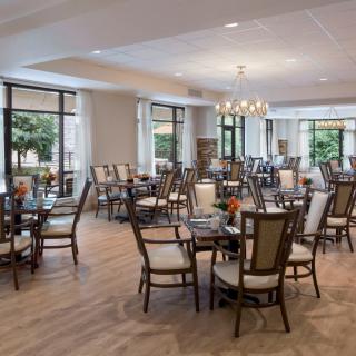 A spacious and elegantly decorated dining room with modern tables and chairs, featuring large windows and a chandelier.