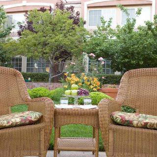 A cozy outdoor seating area with wicker chairs and a table, surrounded by lush greenery and flowers.