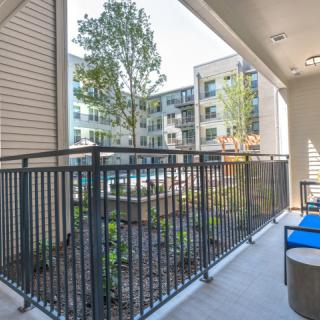 A modern apartment balcony with outdoor seating overlooking a well-maintained courtyard.