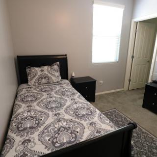 A cozy bedroom featuring a single bed with decorative bedding and black furniture.