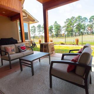 A cozy outdoor patio with cushioned seating and a table, overlooking a backyard with trees.