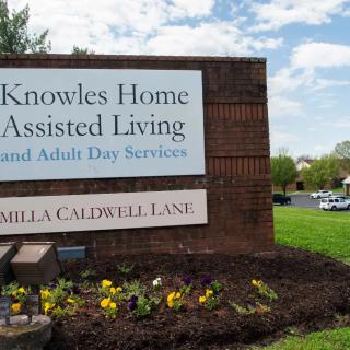 Sign for Knowles Home Assisted Living near a landscaped area with flowers.
