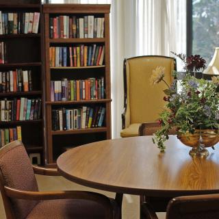 A cozy library corner with bookshelves, a round wooden table, and comfortable chairs.