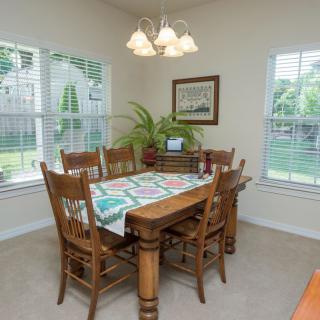 A cozy dining room with wooden furniture and a quilted table runner, illuminated by natural light from the windows.