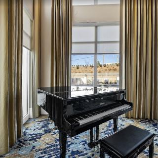 A grand piano positioned in a well-lit room with large windows and elegant curtains.