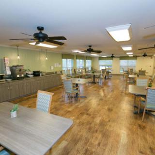 A spacious and well-lit dining area with wooden flooring, featuring several tables and chairs.