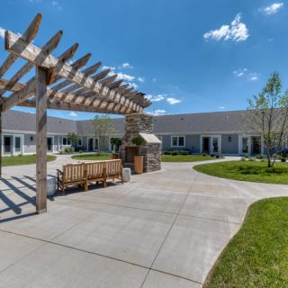 A serene courtyard featuring a pergola with benches and a paved walkway under a clear blue sky.