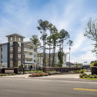 A modern residential apartment complex with surrounding trees and a street in the foreground.