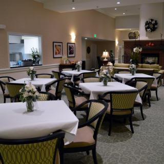A well-decorated dining room with multiple tables and chairs, featuring floral centerpieces and soft lighting.