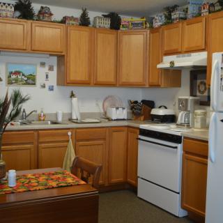 A cozy kitchen featuring wooden cabinets, a stove, refrigerator, and countertop with various appliances and decorations.