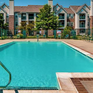 Outdoor swimming pool at an apartment complex with surrounding buildings and a clear sky.