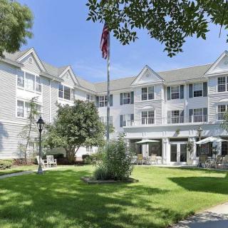 A three-story residential building with a well-maintained garden and an American flag outside.