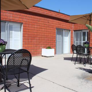 A sunny outdoor patio with tables, chairs, and large umbrellas next to a brick building.
