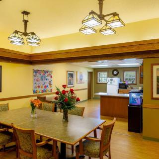 A cozy dining room with a wooden table, chairs, and decorative lighting, featuring a kitchen area in the background.