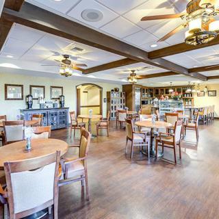 A spacious dining area with neatly arranged tables and chairs, featuring wooden flooring and elegant lighting.