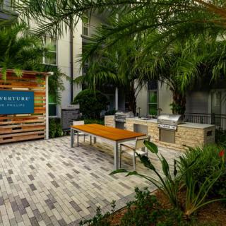 A modern outdoor barbecue area with grills, tables, and lush tropical greenery.