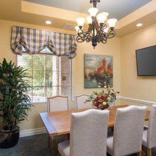 A cozy dining room with elegant furnishings, featuring a chandelier, a large window with plaid curtains, and a decorative plant.