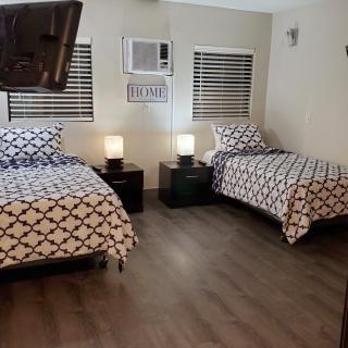 A cozy bedroom featuring two twin beds with patterned bedding, nightstands with lamps, and an air conditioner above the windows.