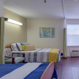 A well-lit hospital room with multiple beds featuring colorful bedding and minimalistic decor.