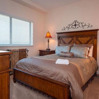 A cozy bedroom with a wooden bed frame, soft linens, and warm lighting.