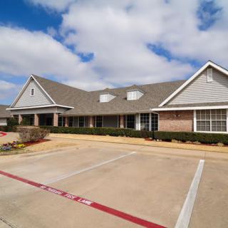 A suburban residential building with a large driveway and parking lot under a partly cloudy sky.