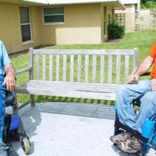 Two people in wheelchairs having a conversation outdoors near a bench.
