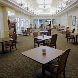 An empty dining area with neatly arranged tables and chairs, featuring chandeliers and a bright interior.