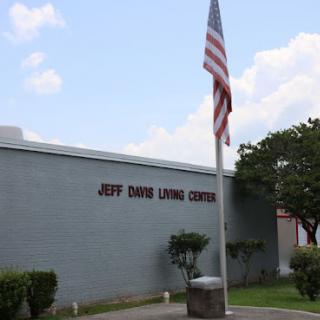 The Jeff Davis Living Center surrounded by greenery, with an American flag proudly displayed.