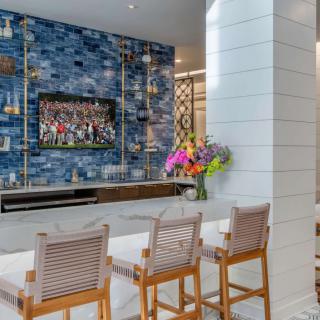 A modern living room featuring a blue tile accent wall with a mounted television, complemented by bar stools and a vibrant flower arrangement.