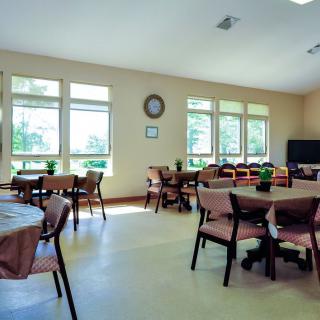 A spacious dining area with multiple tables and chairs, well-lit by natural light through large windows.