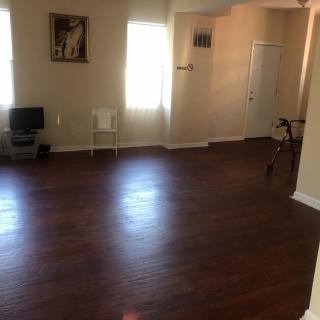 A spacious living room with hardwood floors, minimal furniture, and natural light.
