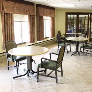 A spacious and well-lit room featuring several round tables and chairs, designed for gatherings or activities.