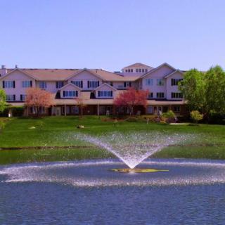 A scenic view of a building with a fountain in the foreground, surrounded by lush greenery.