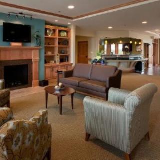 A cozy living room with a sofa and armchairs arranged around a fireplace, television, and bookshelves.