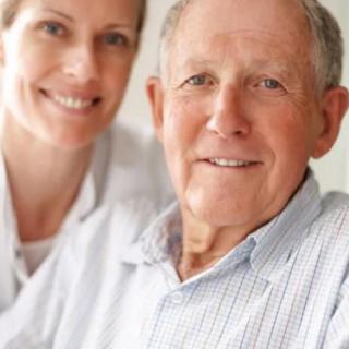 An elderly man smiling with a supportive woman next to him.