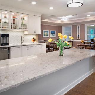 A modern kitchen with a marble countertop, flowers, and an adjacent dining area.