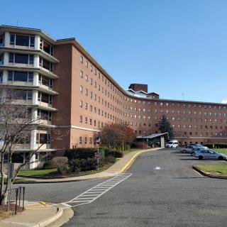 A large hospital building with a parking area in front under a clear blue sky.