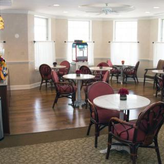 A cozy cafe interior with several tables and chairs, wooden flooring, and large windows providing natural light.