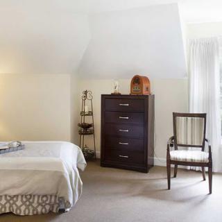 A cozy bedroom with a bed, dark wood dresser, and a classic chair.