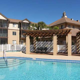 A sunny day view of an apartment complex with a swimming pool and pergola.