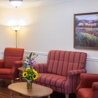 A cozy living room with red upholstered furniture, a wooden table with a vase of flowers, and a painting on the wall.