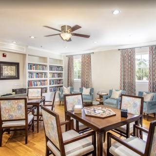 A cozy library room with wooden furniture, a table for board games, and bookshelves filled with books.