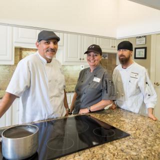 A group of three chefs standing together in a professional kitchen setting.