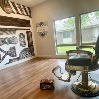 Stylish barbershop interior with a classic barber chair, artistic wall decor, and natural light from large windows.
