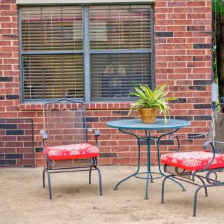 A cozy patio setup with a small round table, red-cushioned chairs, and a potted plant against a brick wall.
